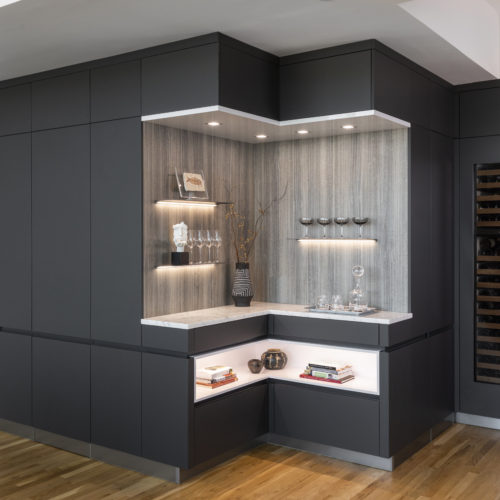 alt="corner view of bar nook with carbon gray matte lacquer cabinets and arctic white paneling with open shelves and integrated LED strip lighting"
