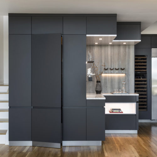 alt="Front view of bar nook and integrated pantry with carbon gray matte satin lacquer cabinets and gloss arctic white paneling"