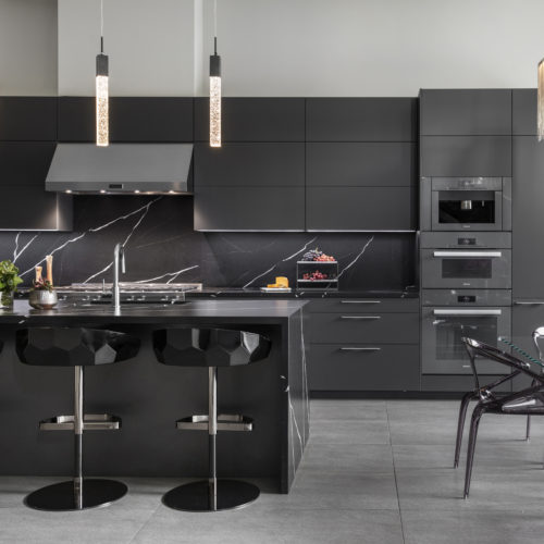 alt="Full kitchen view of carbon gray matte satin lacquer cabinets, appliances, and island with bar seating"