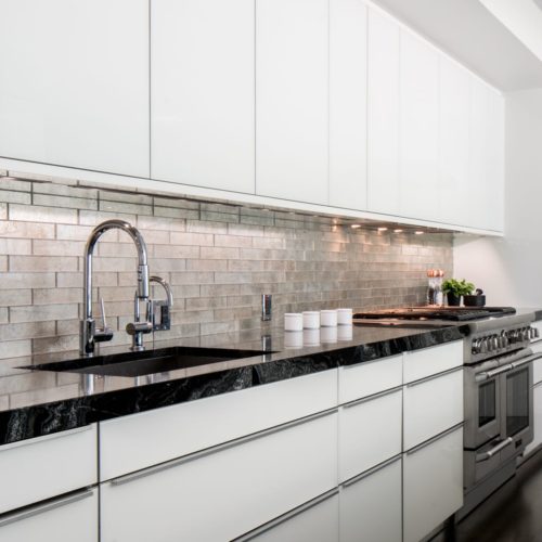 alt="Side view of kitchen showing faucet and stove top as well as IOS white glass cabinets"