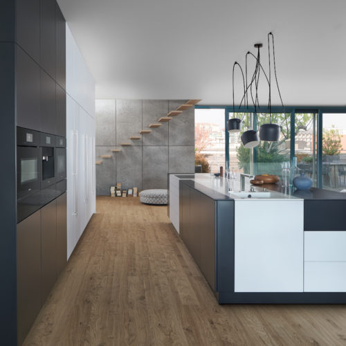 alt="Side view of full kitchen with velvety-feel dark matte-lacquered surface contrasted by anti-finger print white matte-lacquer worktop and floor to ceiling cabinets"