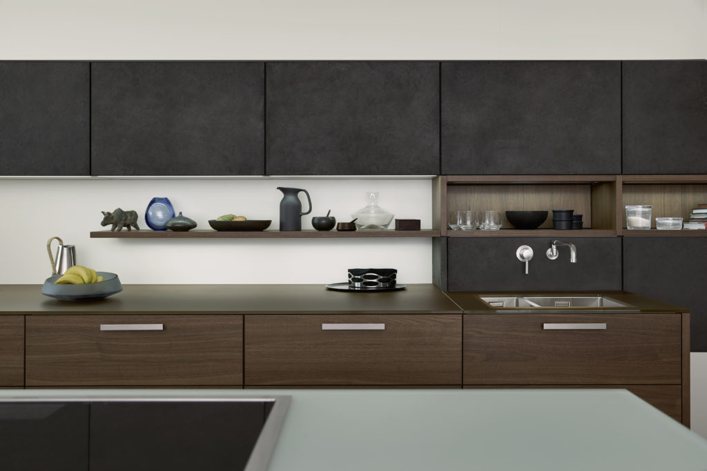 alt="Partial kitchen view of upper cabinets with concrete surface and lower island drawers with TOPOS wood veneer in walnut"
