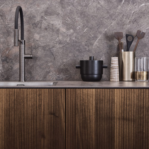 alt="close up view of NASCA backsplash and worktop, steel faucet, and partial view of KERA cabinets with Walnut BOSSA fronts"