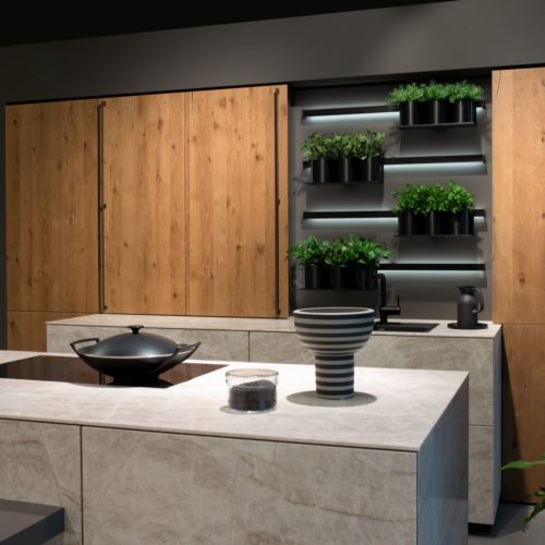 alt="Partial side view of double island with ROCCA fronts contrasting the dark gray walls and MADERO oak veneer cabinets"