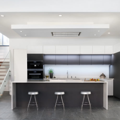 alt="Front view of kitchen showing island with integrated table top, carbon gray matte door panels and frosty white upper cabinets"