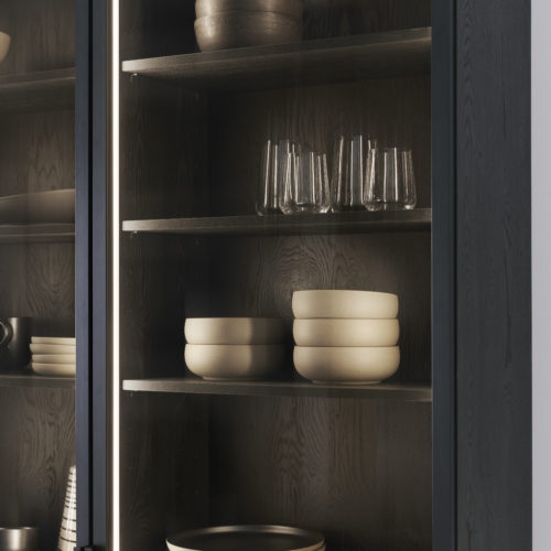 alt="expanded view of upper dark wood cabinet, smoked glass, inset lighting, and LEICHT handles"